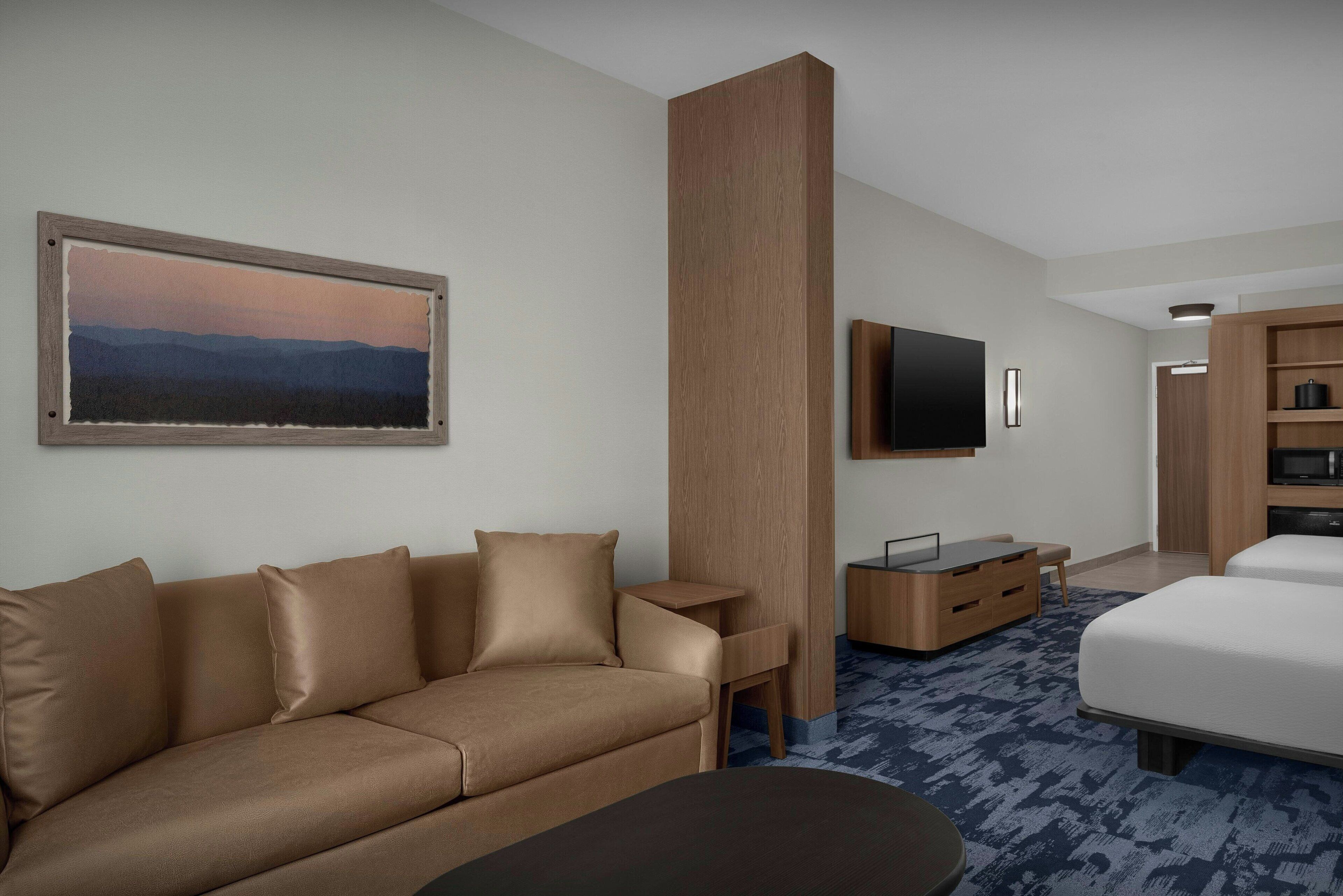 A modern hotel room with a sofa, a bed, a flat-screen TV, a wooden desk, and a large painting on the wall.