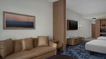 A modern hotel room with a sofa, a bed, a flat-screen TV, a wooden desk, and a large painting on the wall.
