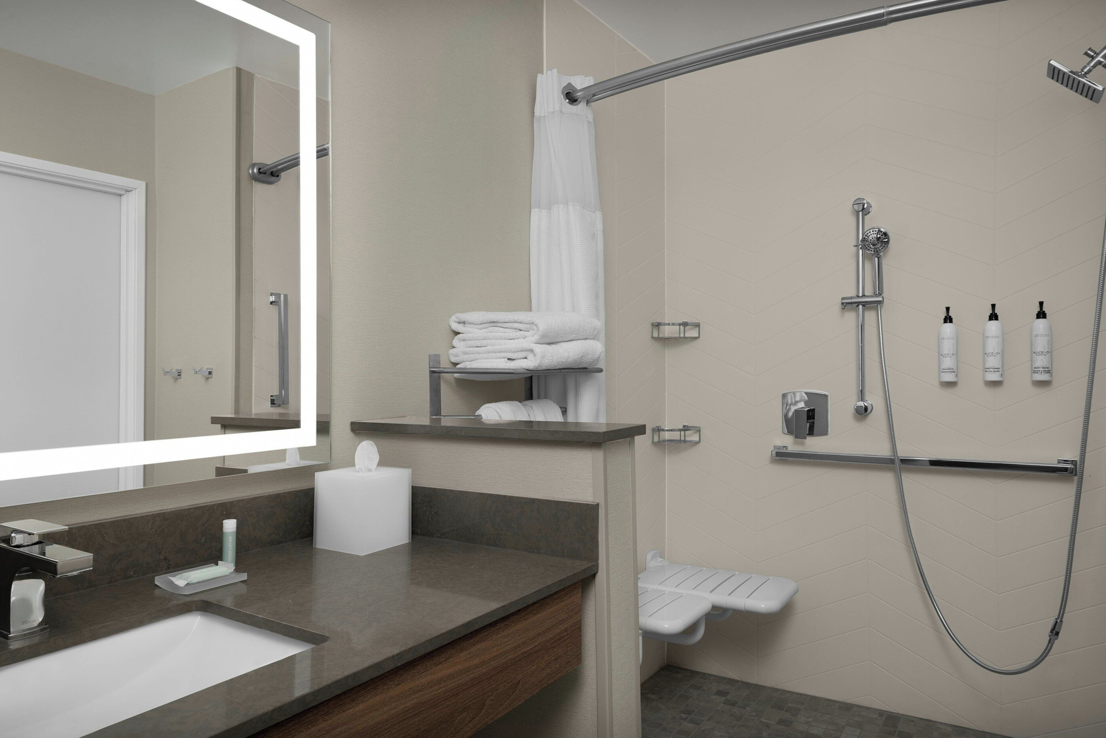 Une salle de bain moderne avec un grand miroir, un lavabo, une douche équipée d’un pommeau de douche à main et des serviettes soigneusement pliées.