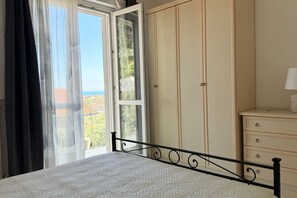 A bedroom with a bed, a wardrobe, and a window with curtains. - Villa Lyla - Marcelli, elegant villa with garden overlooking the sea (Marcelli)