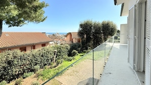 Un balcón con vistas al mar, un jardín y un edificio con techo de tejas.