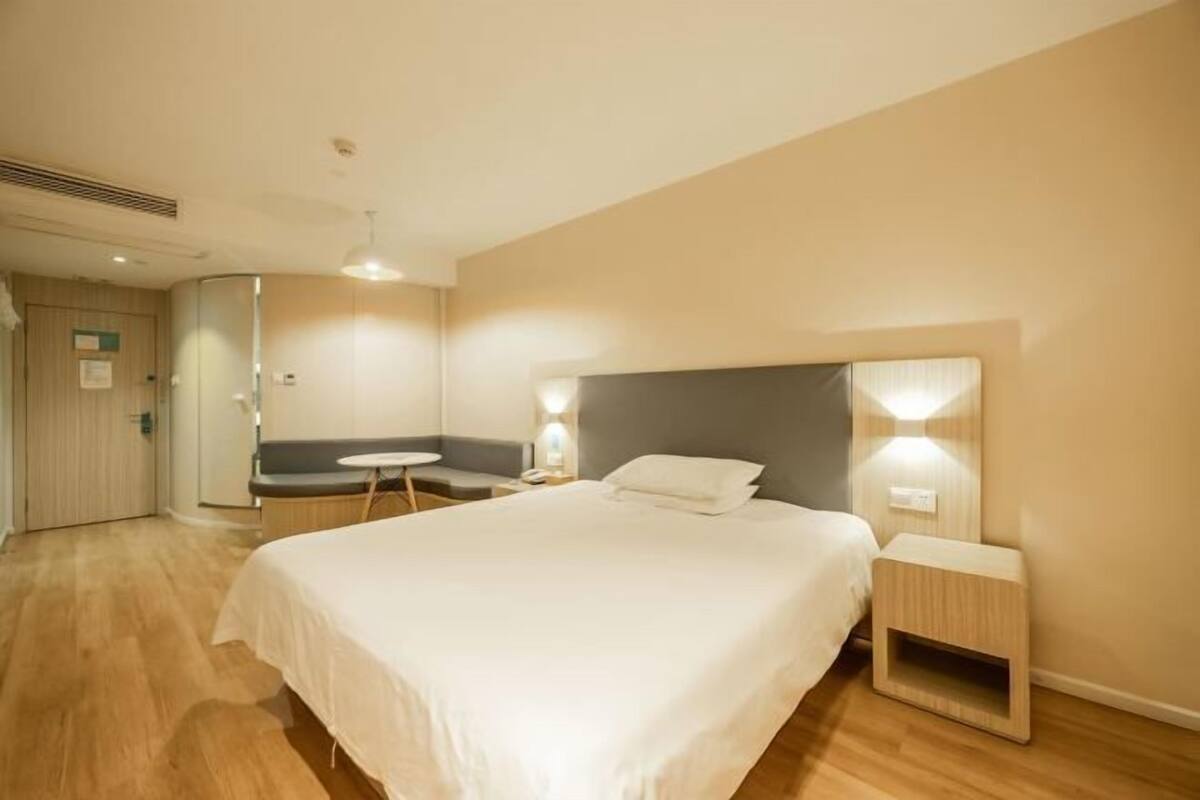 A hotel room with a large bed, bedside tables, a small round table, and a seating area with a bench.