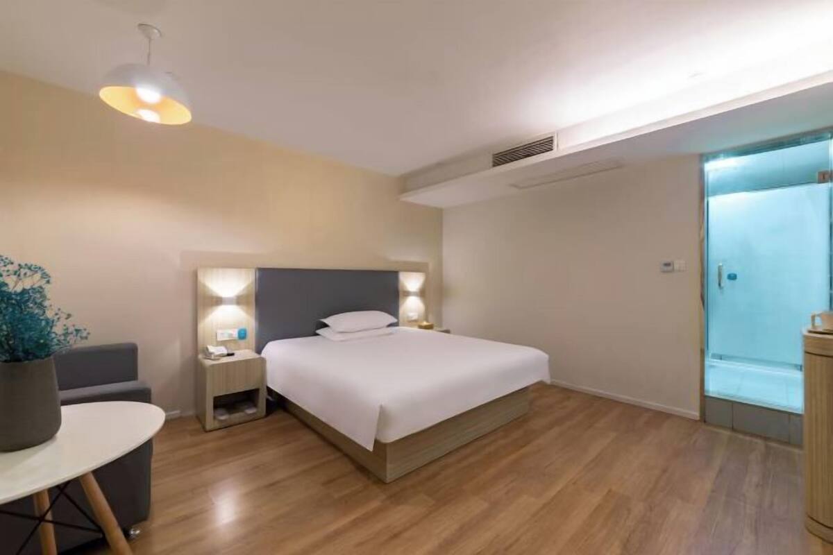 A modern hotel room with a bed, bedside tables, a small table, and a potted plant.