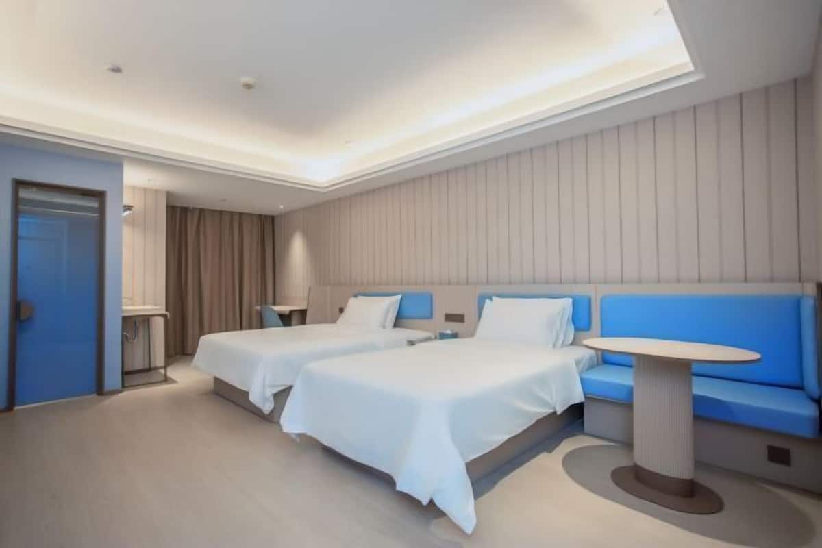 Une chambre d’hôtel moderne avec deux lits, un canapé bleu, une table ronde et une porte sur le côté gauche.