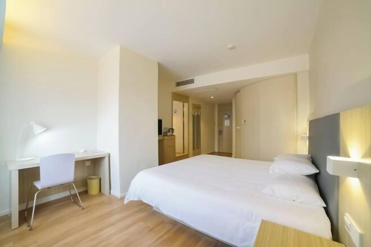 A hotel room with a bed, a desk, a chair, and a small trash bin.