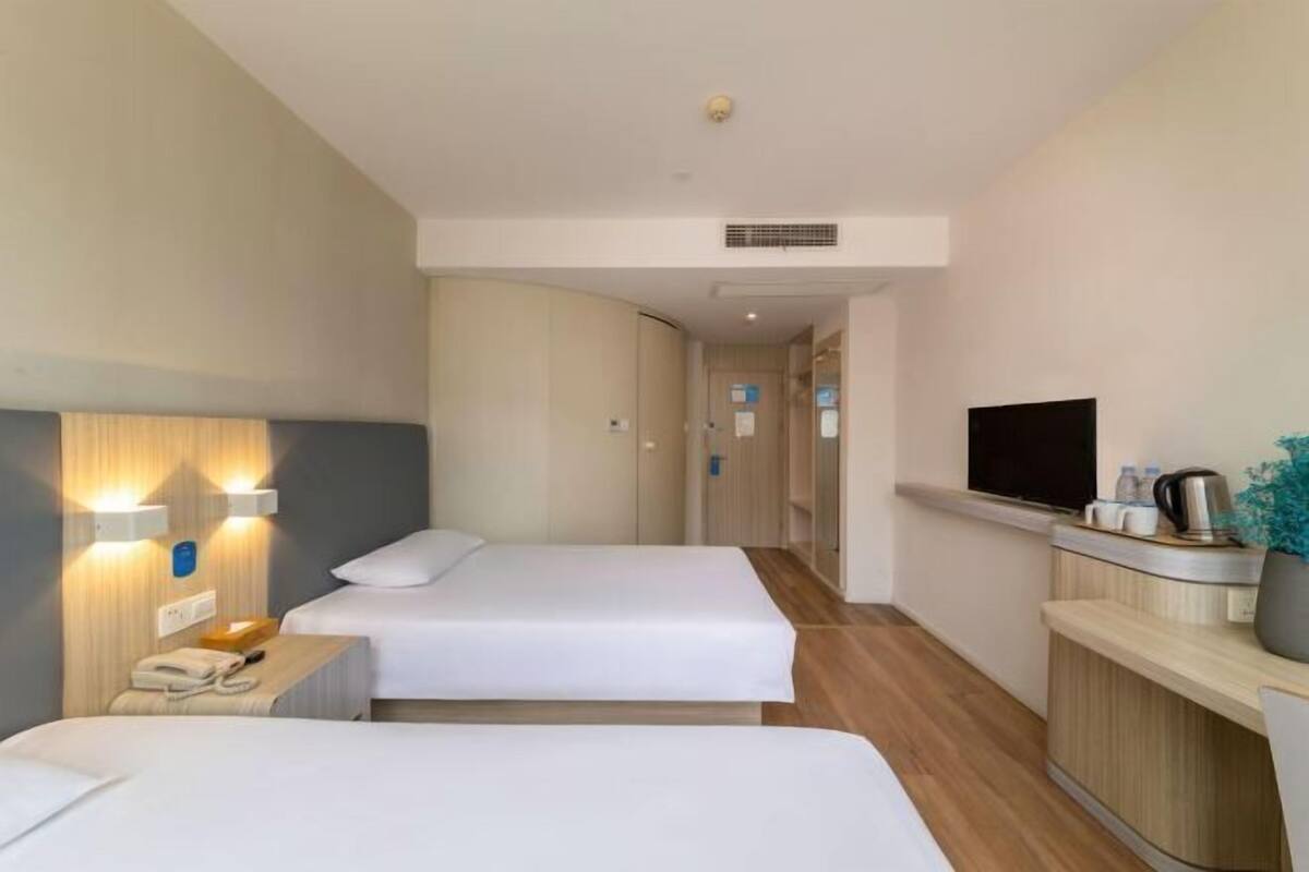 A hotel room with two beds, a TV, a desk with a phone, and a kitchenette.