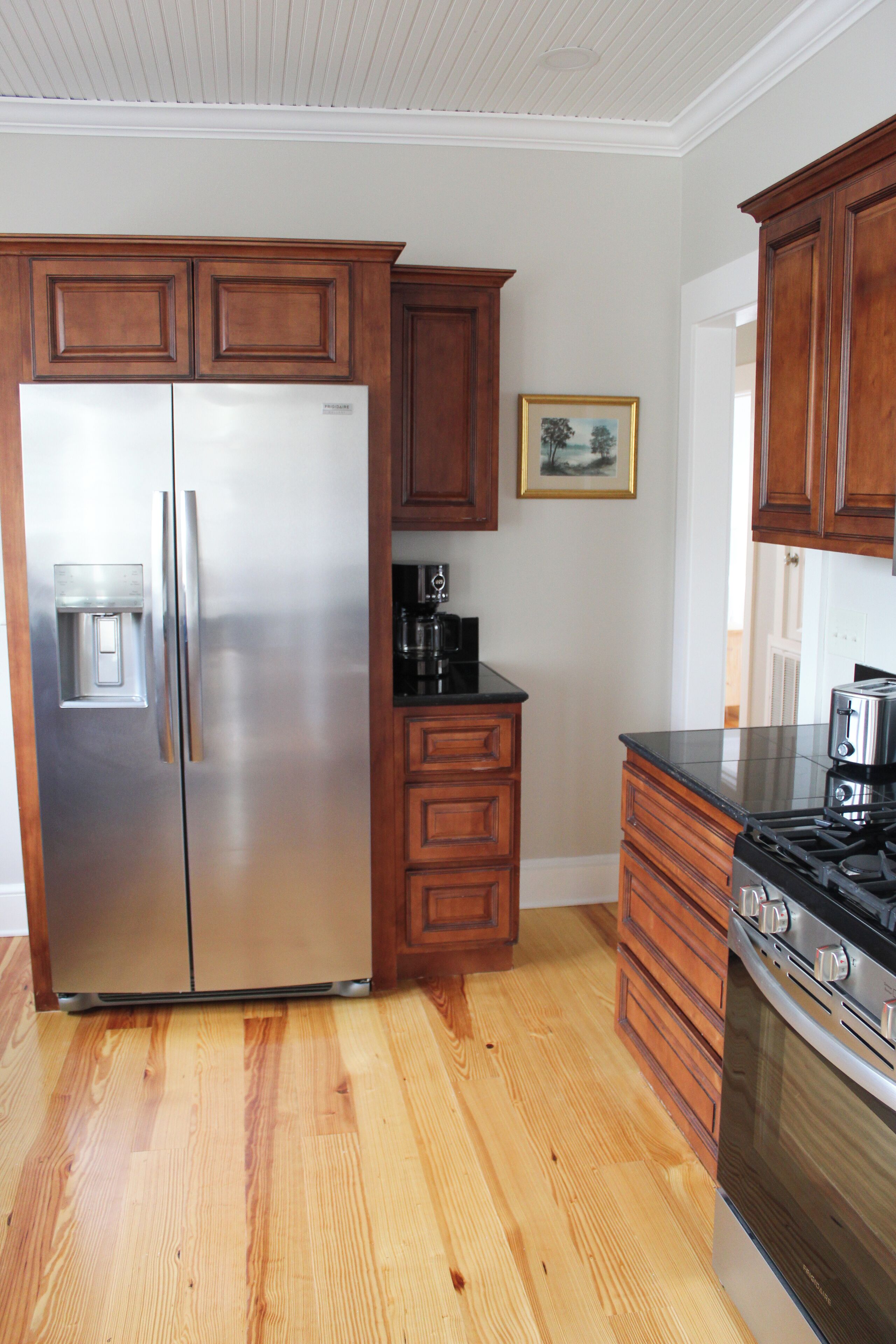 A kitchen with wooden cabinets, a stainless steel refrigerator, a stove, and a coffee maker.
