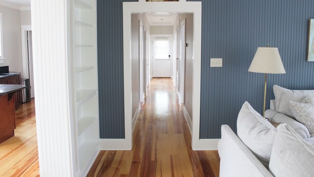 Un pasillo con suelo de madera, un sofá blanco y una lámpara.