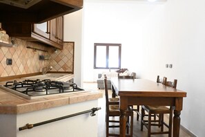 A kitchen with a gas stove, wooden cabinets, a dining table with chairs, and a window providing natural light.