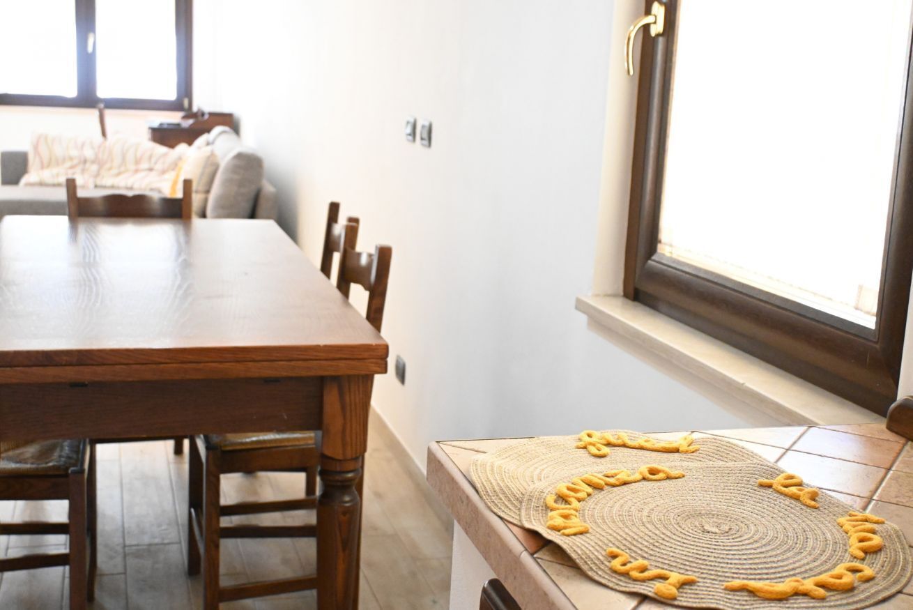 A dining area with a wooden table and chairs, a woven placemat with yellow shapes, and a window with a view of the outside.