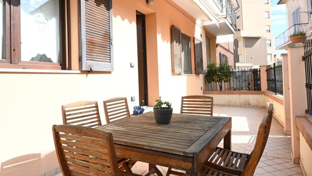 A wooden table with chairs, a potted plant, and a window with shutters.