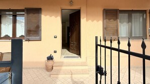 A building entrance with a door, a small step, a potted plant, and a metal gate.