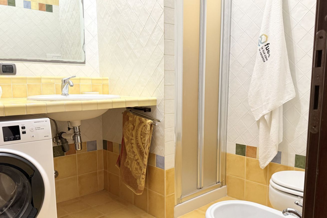A compact bathroom with a washing machine, a sink, a toilet, and a shower area.