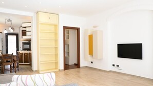 A modern living room with a sofa, a TV mounted on the wall, and a kitchen area in the background.