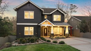 A two-story house with a dark exterior, a front porch, and a stone foundation. - Luxury Charlotte Home with Stunning Pool & Hot Tub & Waterfalls (Charlotte)