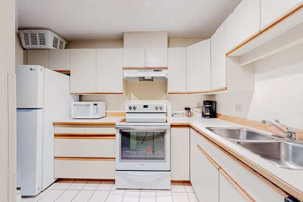 A kitchen with white cabinets, a microwave, an oven, a sink, and a coffee maker. - Foxglove by Whistler Premier (Whistler)