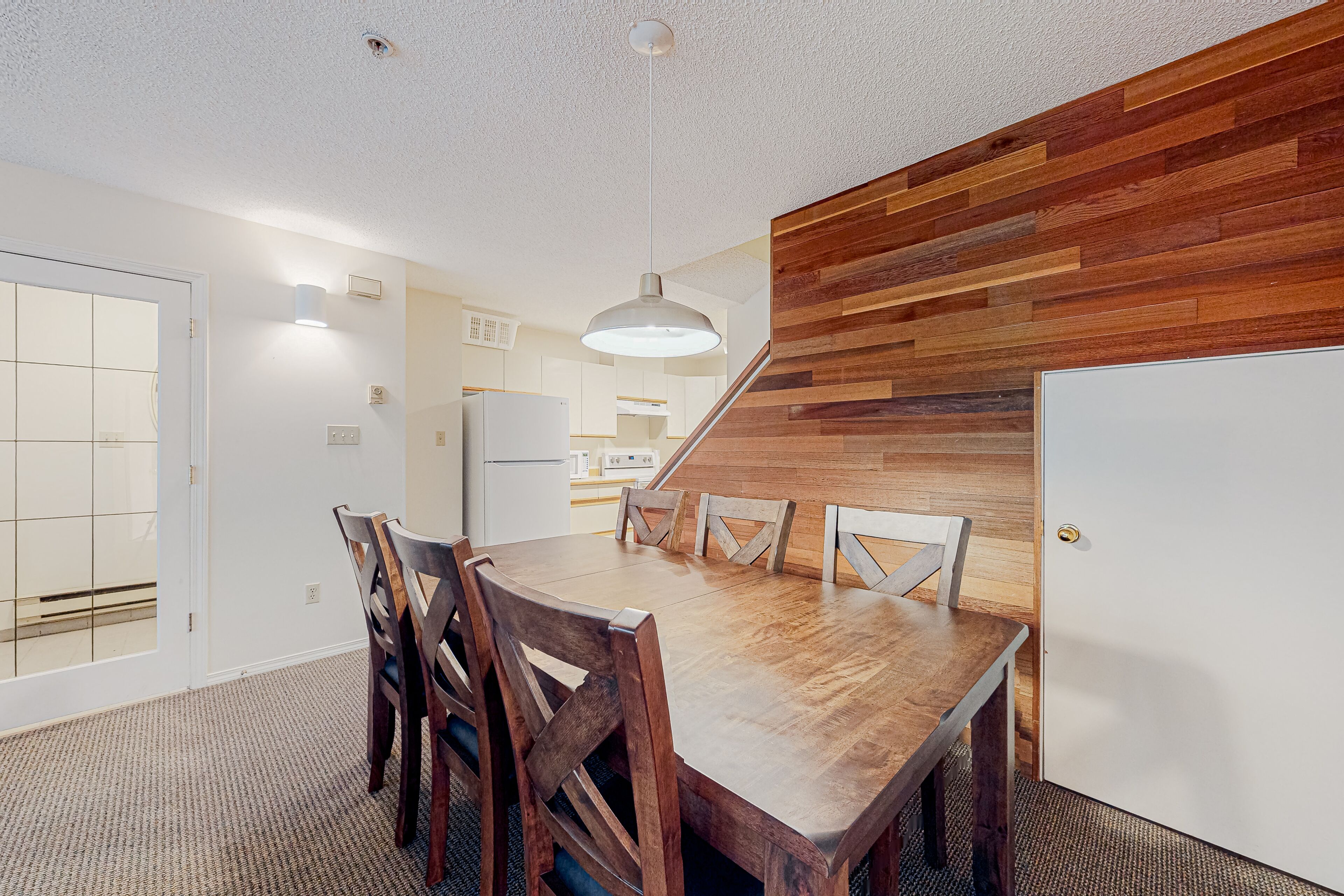 Ein stilvoller Essbereich mit Holztisch und -stühlen, einem weißen Kühlschrank und einer Küche im Hintergrund.