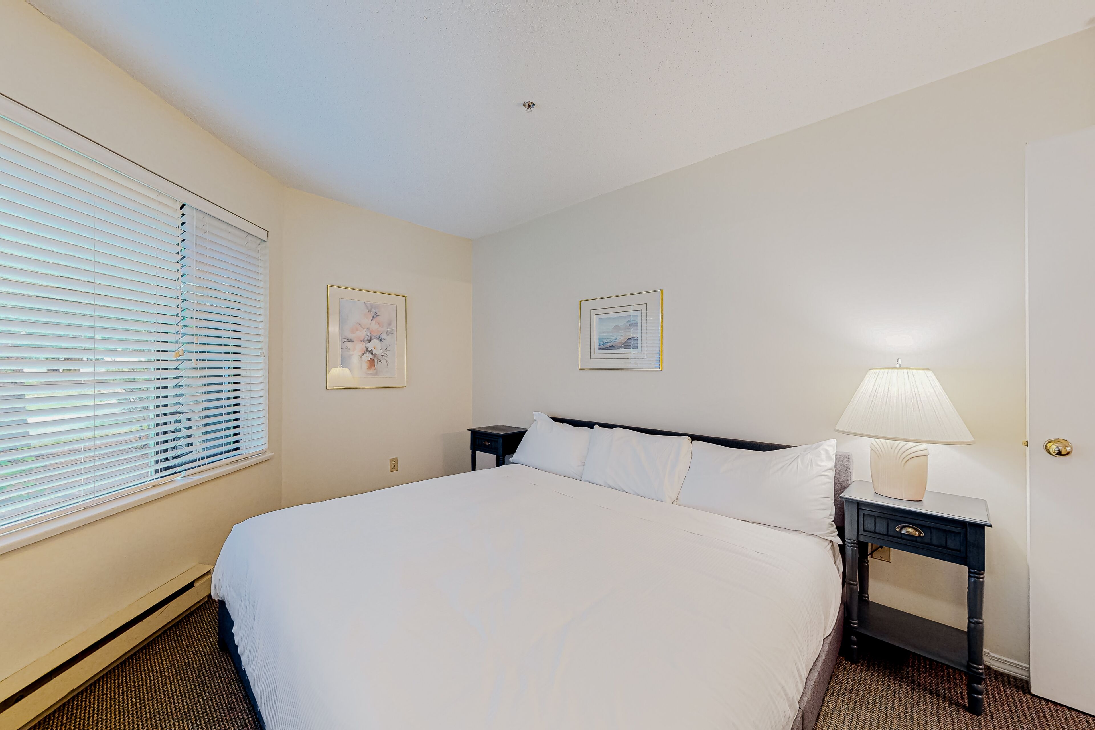 Una habitación de hotel con una cama, una mesita de noche con una lámpara y dos cuadros en la pared.