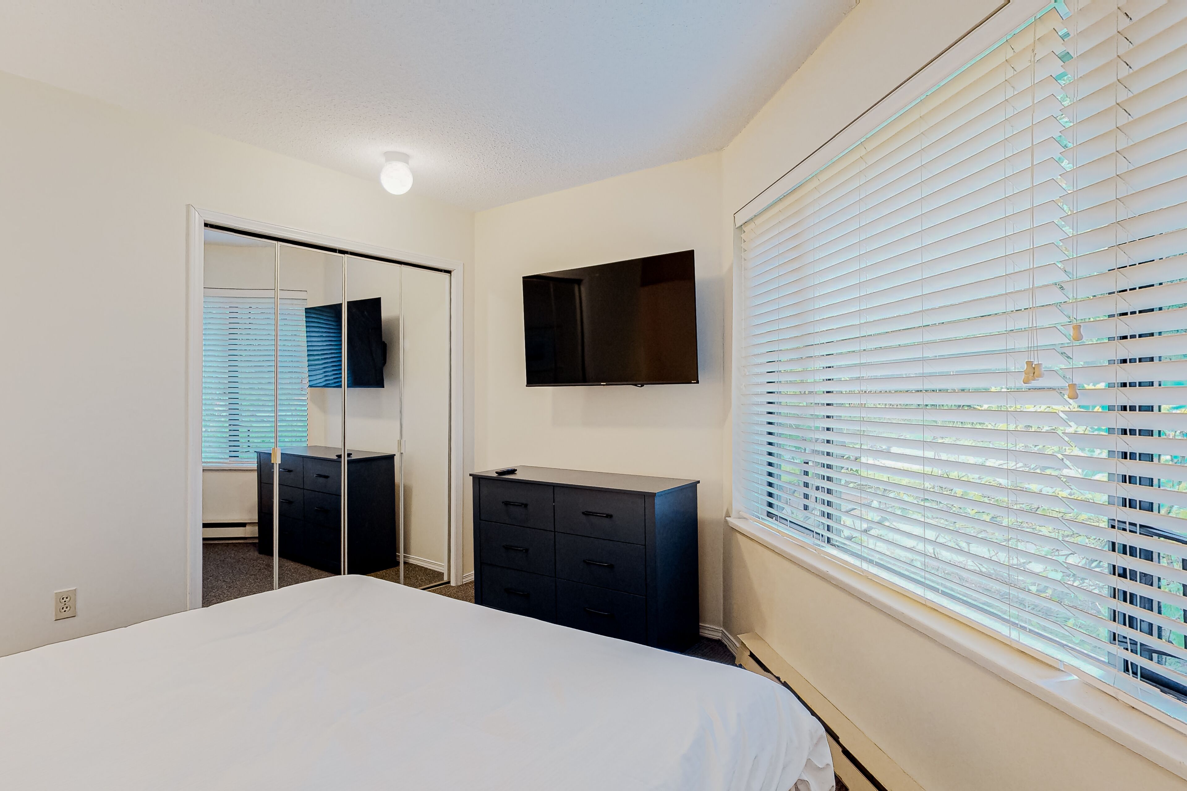 Ein Schlafzimmer mit einem Bett, einem Schminktisch, einem Spiegel und einem an der Wand montierten Fernseher.