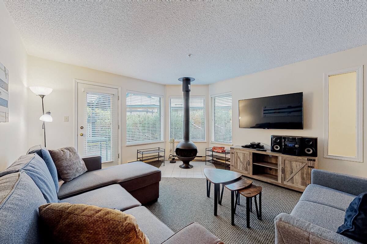 Una sala de estar con sofá, sillón, televisor, parlantes y chimenea.
