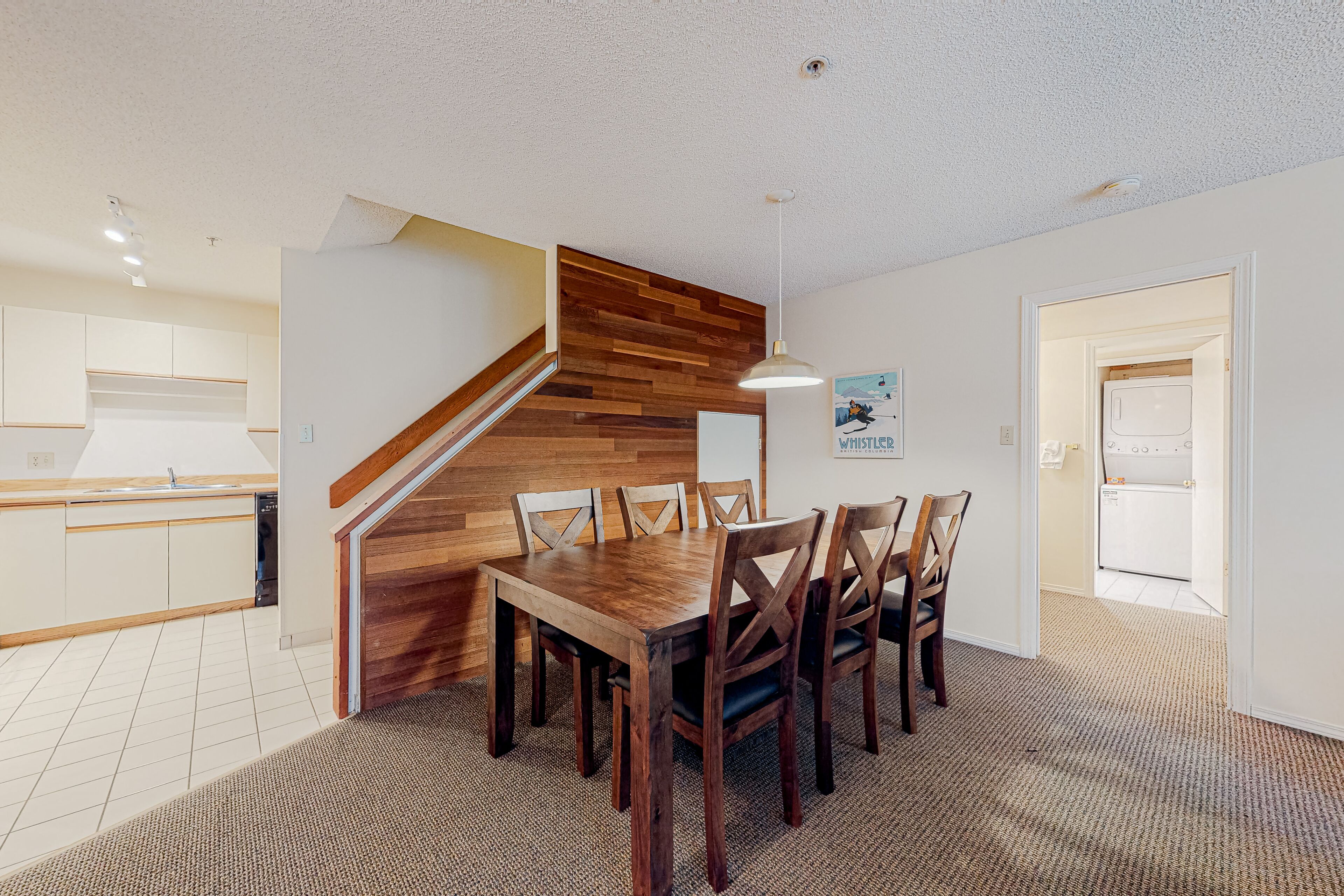 A modern kitchen with white cabinets, a wooden staircase, and a dining area with a wooden table and chairs.