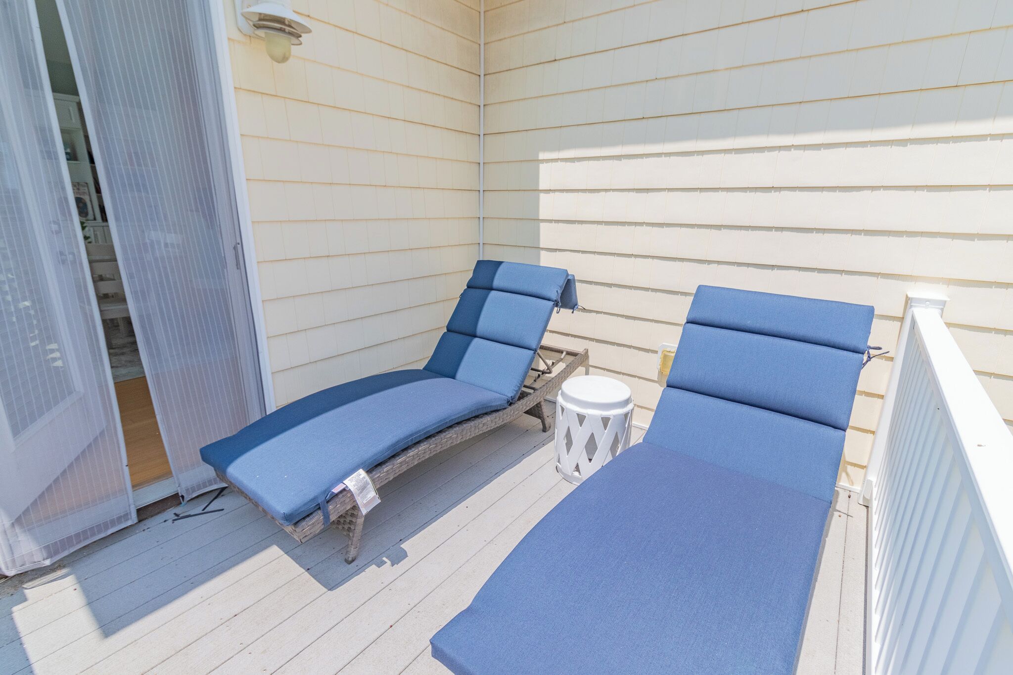 Een overdekt terras met twee blauwe loungestoelen en een witte bijzettafel.
