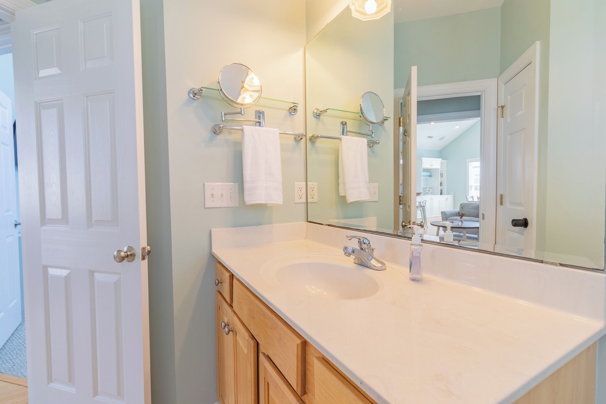 A bathroom with a white sink, two mirrors, and a glass shelf with towels.