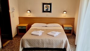 Een hotelkamer met een bed, twee nachtkastjes, een telefoon aan de muur en een ingelijste foto.
