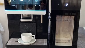 A coffee machine with a digital display menu, a cup, and a water reservoir. - hotel Anny  (Cervia)