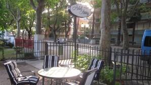 An outdoor seating area with a round table and striped chairs, surrounded by a metal fence, with a sign reading "Hotel Annie" in the background.