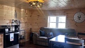 A cozy cabin interior with a wooden interior, a dining table, a sofa, and a kitchen area with appliances. - Charming 2-bedroom cabin minutes from Sacandaga Lake and Saratoga Springs (Amsterdam)