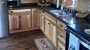 A kitchen with wooden cabinets, a stainless steel refrigerator, a microwave, and a sink. - Charming 2-bedroom cabin minutes from Sacandaga Lake and Saratoga Springs (Amsterdam)