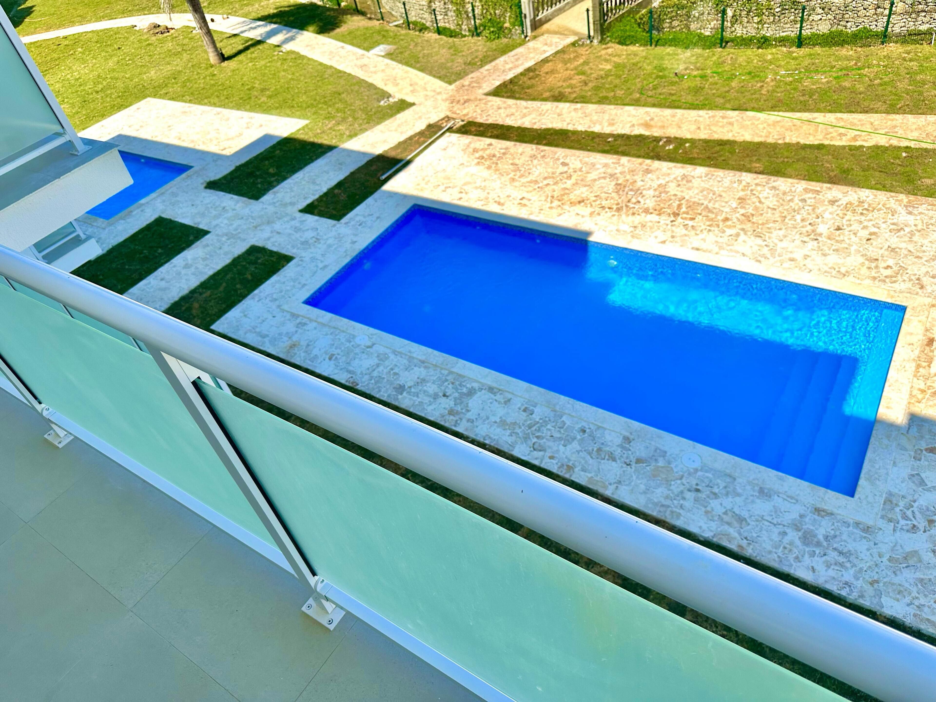A swimming pool with a tiled deck and a glass railing.