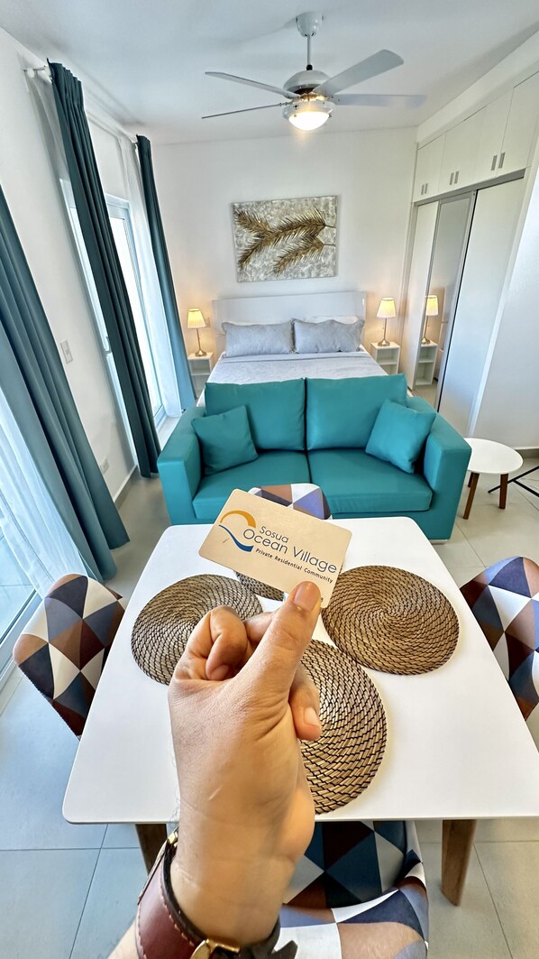 A hotel room with a bed, a teal sofa, a dining table with placemats, and a ceiling fan.