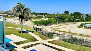 Ein Poolbereich mit klarem, blauem Wasser, umgeben von einer angelegten Gartenanlage mit Palmen und Blick auf eine hügelige Landschaft im Hintergrund.