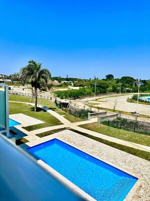 Zona de piscina con agua azul cristalina, rodeada por un jardín ajardinado con palmeras y vistas a un paisaje montañoso al fondo.