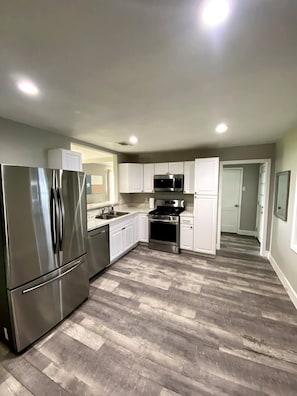 Une cuisine moderne dotée d’appareils électroménagers en acier inoxydable, de meubles blancs et d’un parquet en bois disposé en motif chevron.