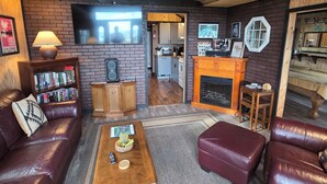 A cozy living room with a fireplace, leather furniture, a bookshelf, and a television. - "That 70's Cottage" (on Lake Erie!) Free Firewood! (Essex)
