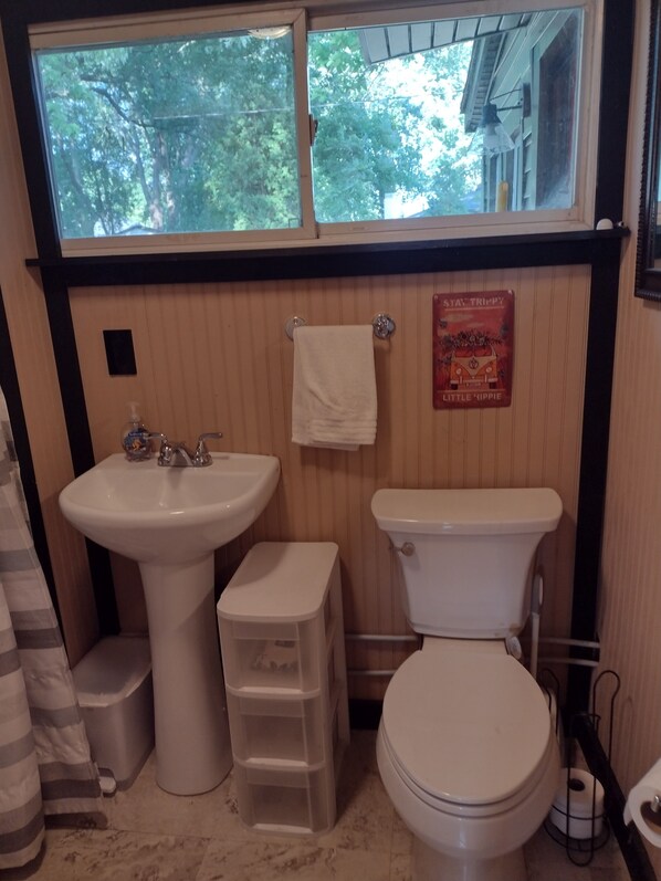 Un baño con ventana, lavamanos, inodoro y cubo de basura.