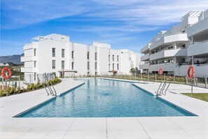 A swimming pool with a clear blue sky, surrounded by white buildings with balconies.