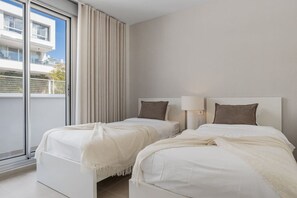 Ein Hotelzimmer mit zwei Betten, einem großen Fenster mit Vorhängen und Blick auf ein Gebäude.