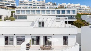 A modern white building with multiple balconies, large windows, and a flat roof.