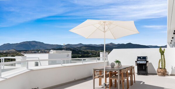 A rooftop terrace with a table and chairs, a grill, and a large umbrella. - Feliz | Roof terrace - pool - gym (Estepona)