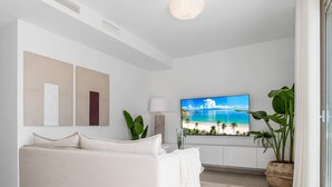 A modern living room with a sofa, a flat-screen TV displaying a beach scene, and a potted plant.