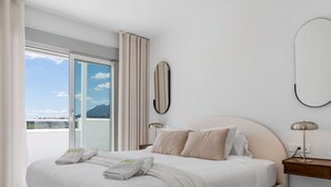 A modern hotel room with a large bed, a nightstand, a lamp, and a view of the mountains through the window.