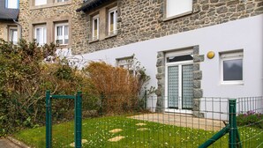 Une maison en pierre à l’extérieur blanc, avec une porte verte et un petit jardin agrémenté de pas japonais.