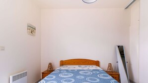 Une petite pièce, peu meublée, avec un lit simple, un radiateur, un tableau accroché au mur et une porte sur le côté droit.