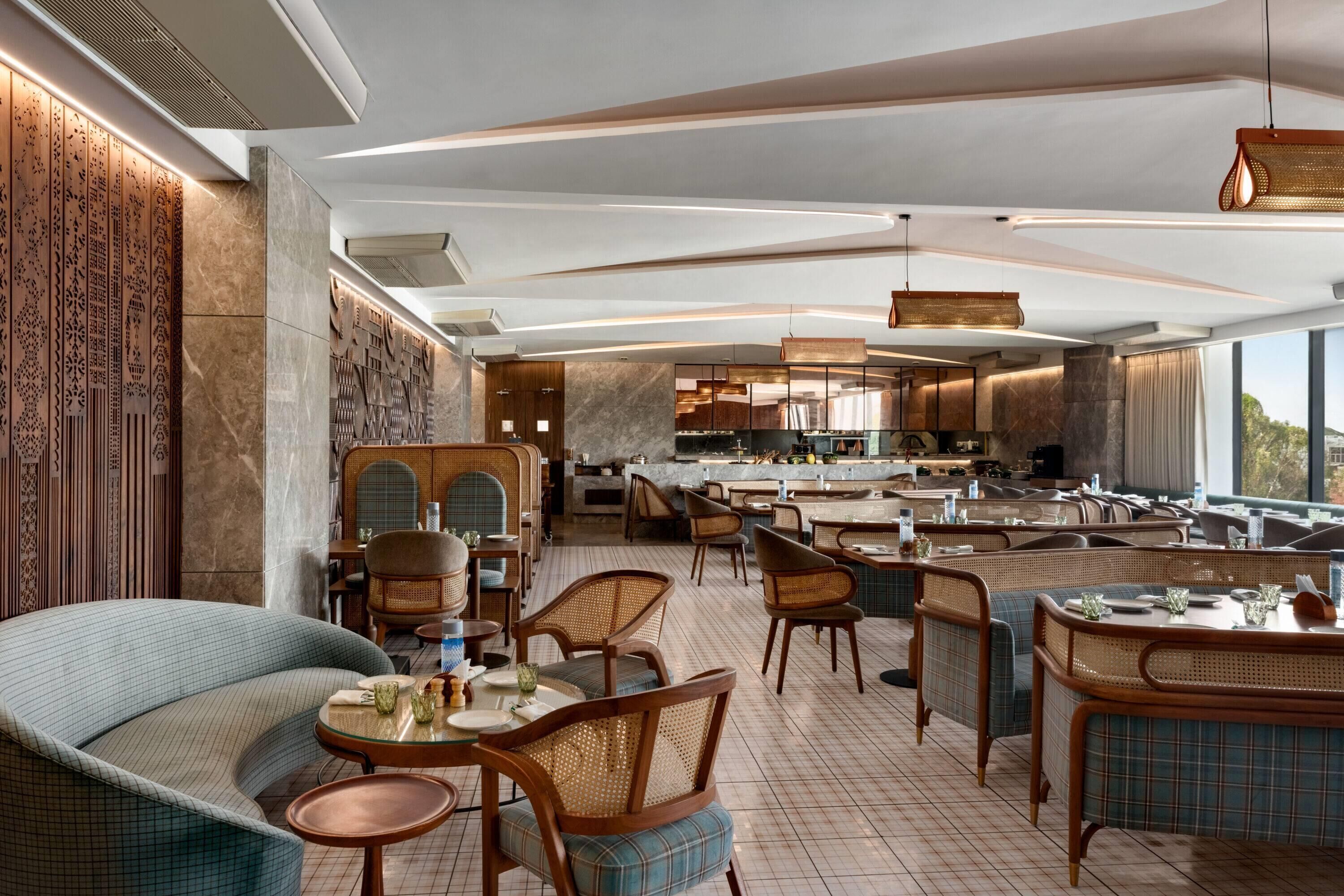 A modern restaurant with a mix of seating options including tables and chairs, a bar area, and a kitchen visible in the background.