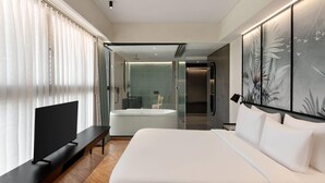 A modern hotel room with a large bed, a flat-screen TV, a bench, a bathtub, and a glass-enclosed shower area. - Ramada Encore By Wyndham Ambala Gt Road (Ambala)