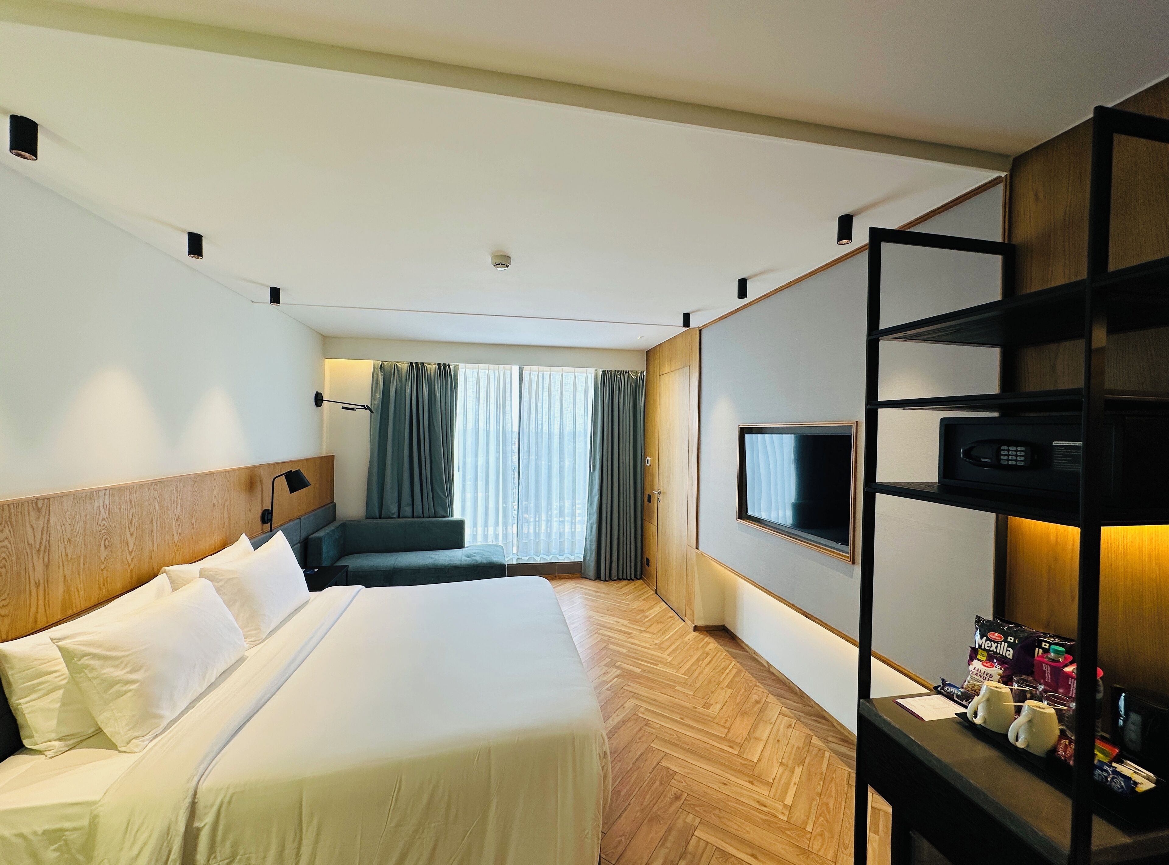 A hotel room with a large bed, a desk with a TV and microwave, and a view of the city through the window.